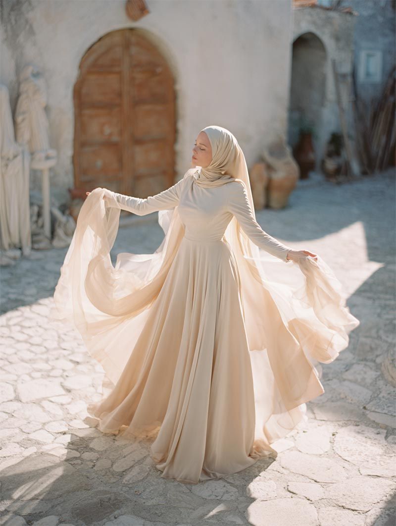 A bride in a flowing gown with a hijab dances on a cobblestone street at her luxury wedding destination in Rome, Italy