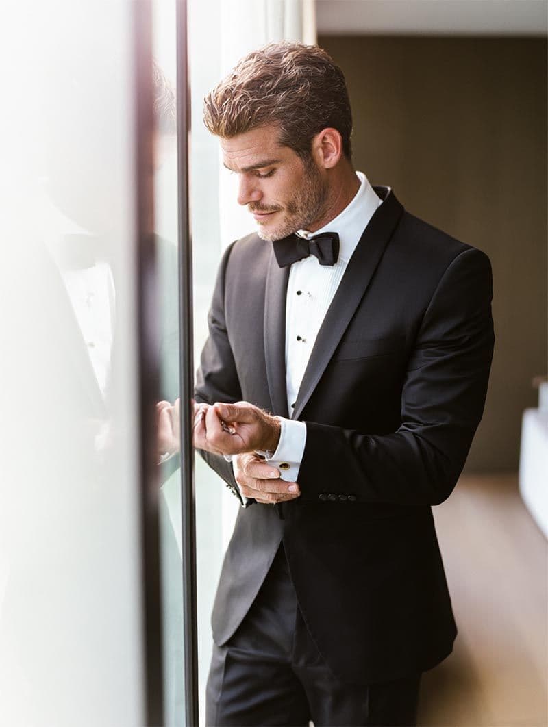 Groom adjusting cufflinks in soft natural light, editorial getting-ready detail